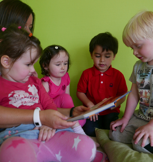 Bild Siloah Kindertagesstätten, Kindergartengruppen, 4 Kinder sind im Kreis, Erzieherin liest aus einem Buch vor